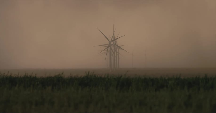 Row of wind turbines rotate slowly forming a spiky group in dense fog