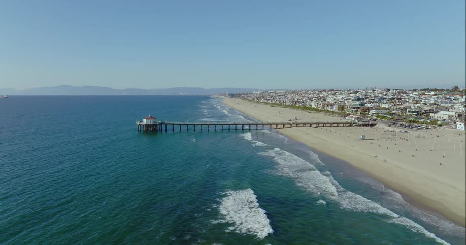 People move about beach near pier bordering apartment buildings as waves roll onto shore