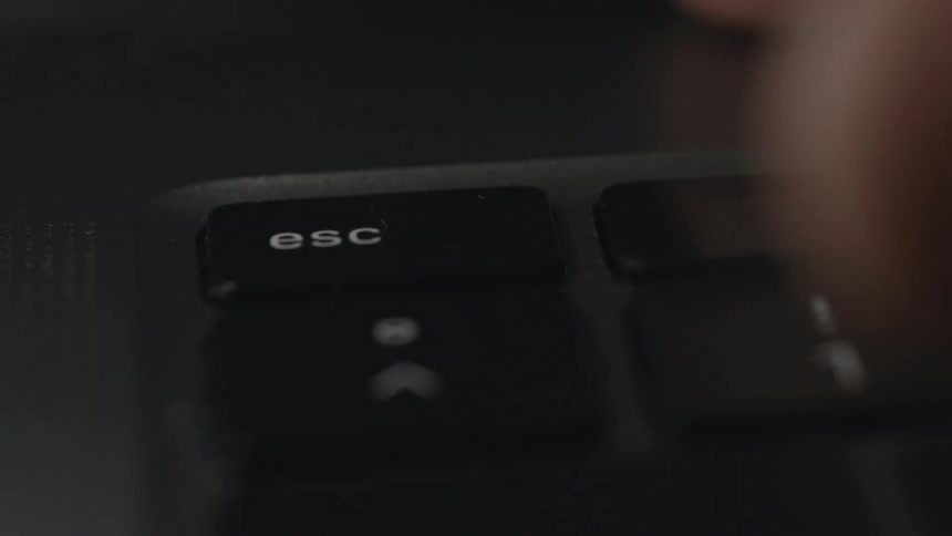 A person uses a finger to press the escape key on a computer keyboard