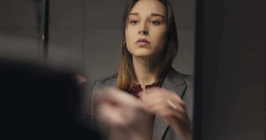 A woman puts on a suit jacket in her bedroom mirror