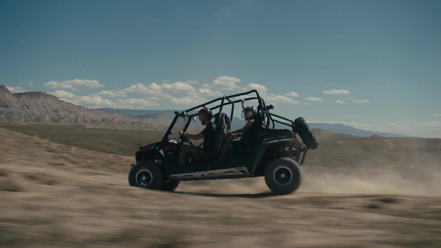 Four people with helmet drives off road vehicle across the plain