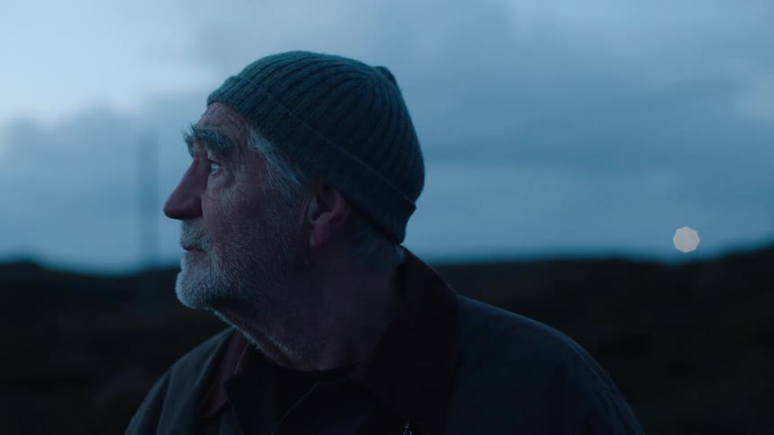 An elderly man wearing a knit beanie looks around at his surroundings before starting to walk away