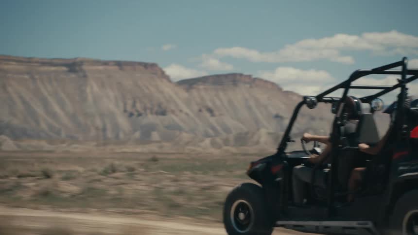 Four people riding in a dune buggy through a desert landscape along a ridge