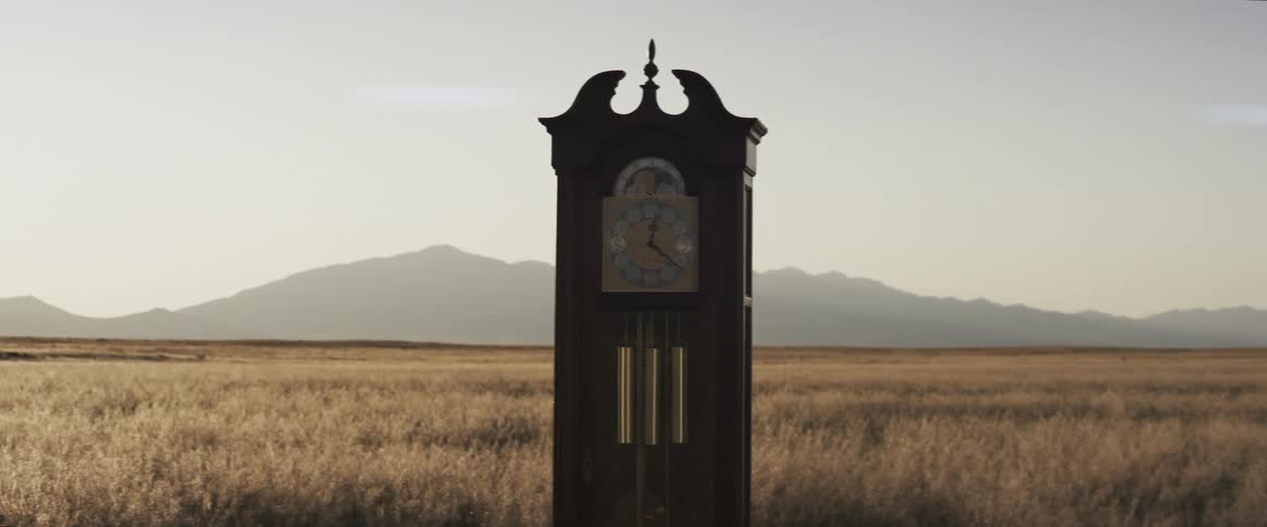 A grandfather clock sits in the middle of an open field