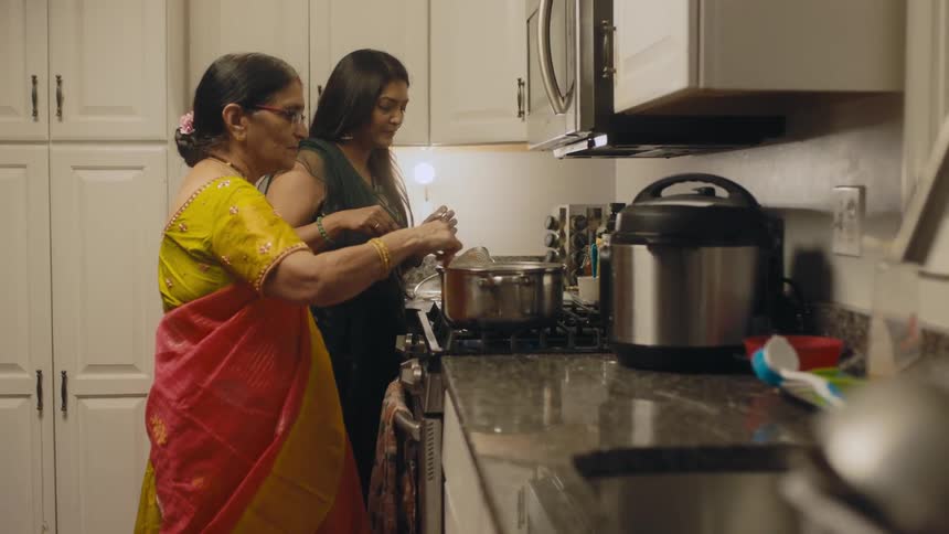 Two indian women stand together in a kitchen while preparing food