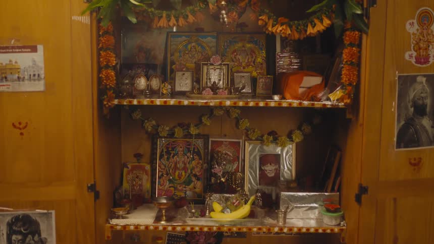 A wooden cabinet with doors open to display the pictures and garland of a home altar