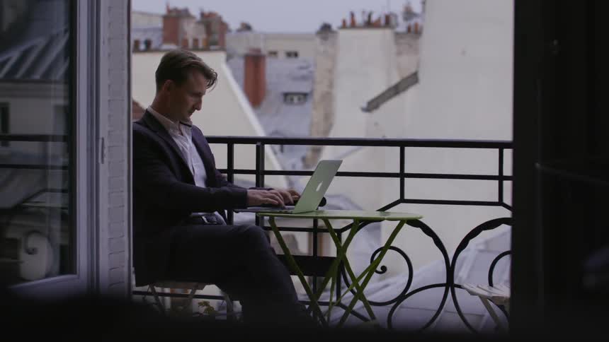 Man works on a laptop on a balcony