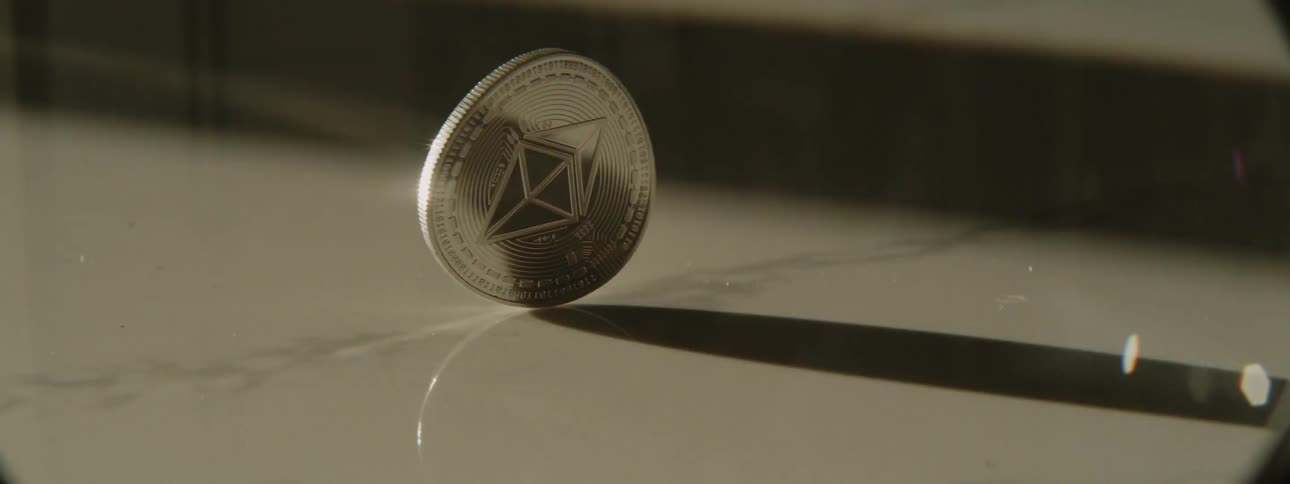 A person spins a large silver coin on the surface of a table