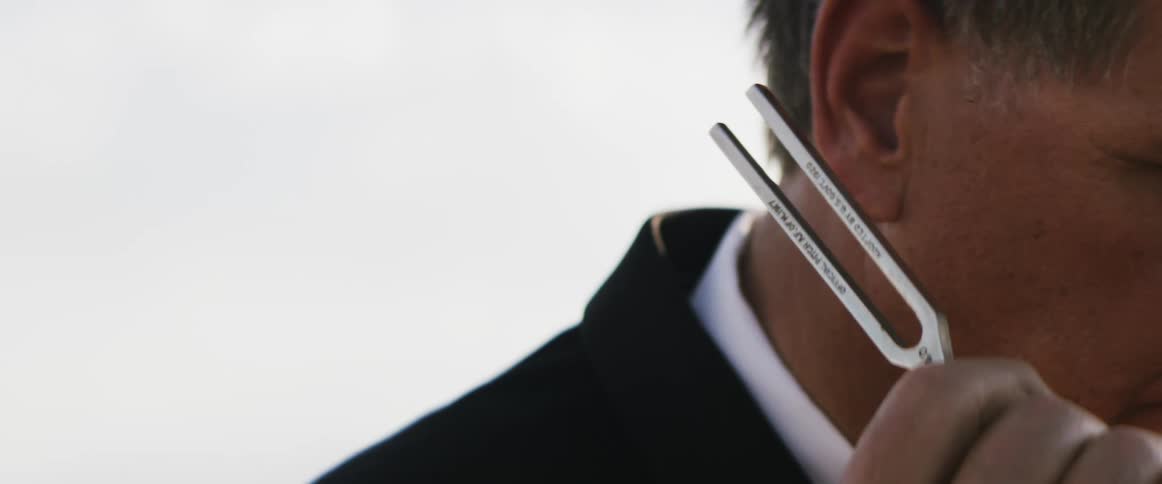 A man is holding a tuning fork near his ear