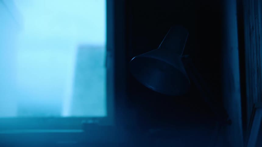 A flexible lamp with metal shade glows dimly and for a brief time near a window