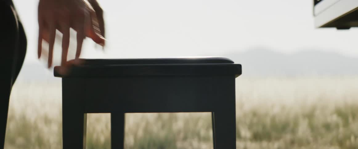 Man in black suit moves stool to play piano in the open field