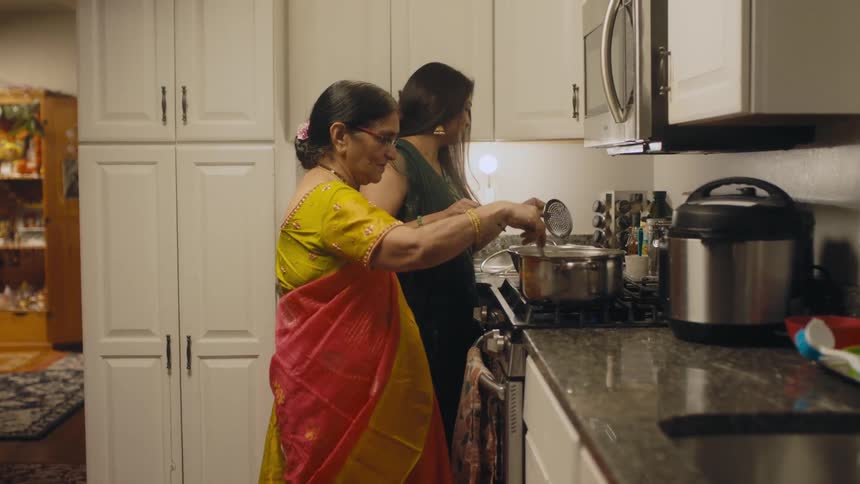Two women are in a kitchen cooking and stirring the pots