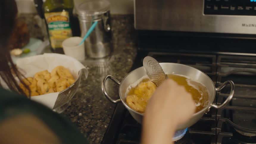 A woman at home stirs bagels as they boil in a pot