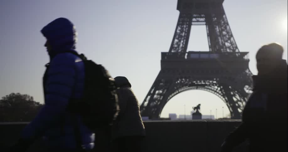 People walking by the base of the eiffel tower on a cold day