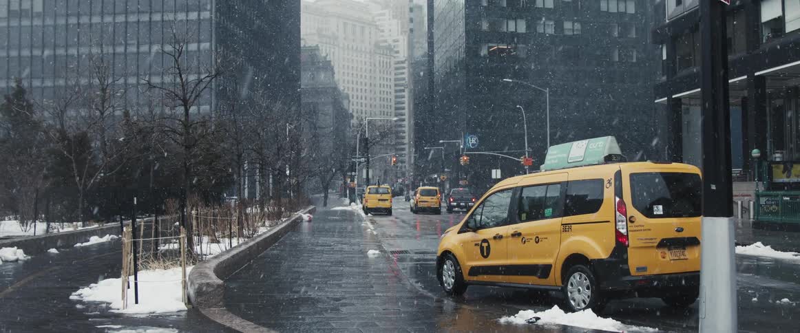A taxi cab parked on the side of a road in a metropolis on a snowy day