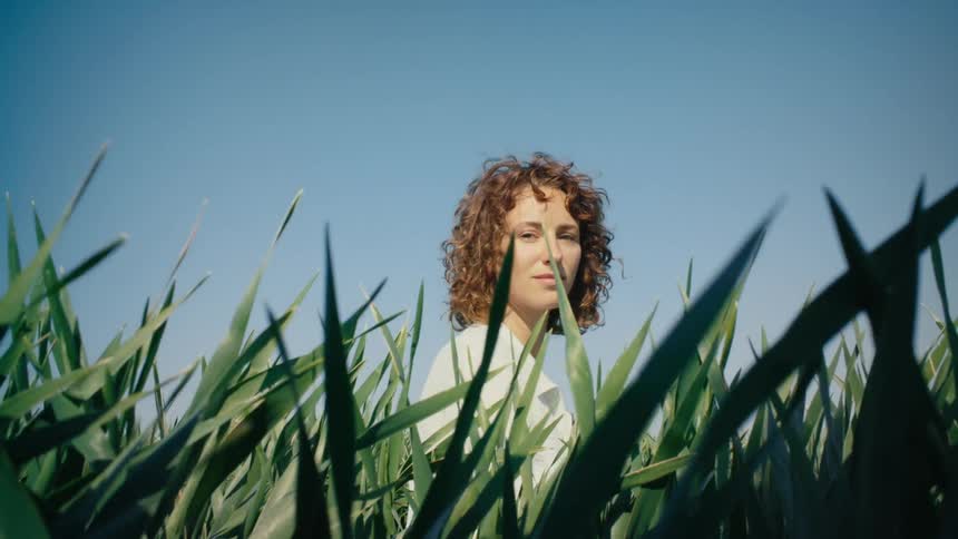 A woman sitting in a green field smiling softly then turning her head