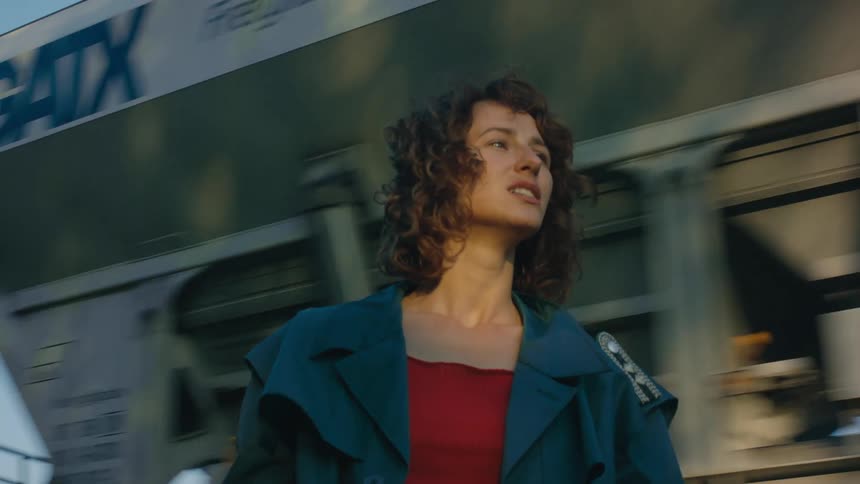 A woman stands outside smoking as a cargo train passes behind her