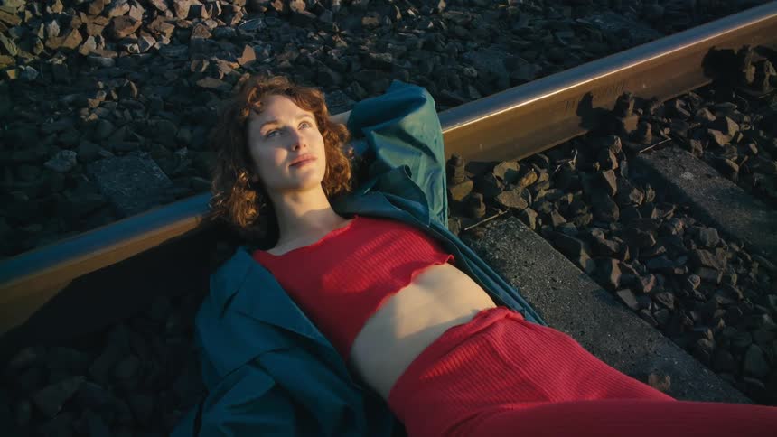 A woman looks up towards the sky as she lies across train tracks