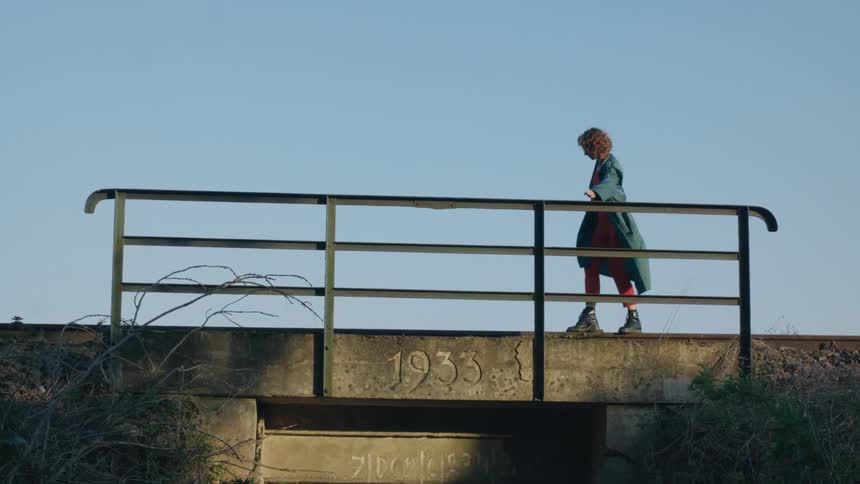 A woman stretches her arms out as she balances herself as she walks across the edge of a bridge