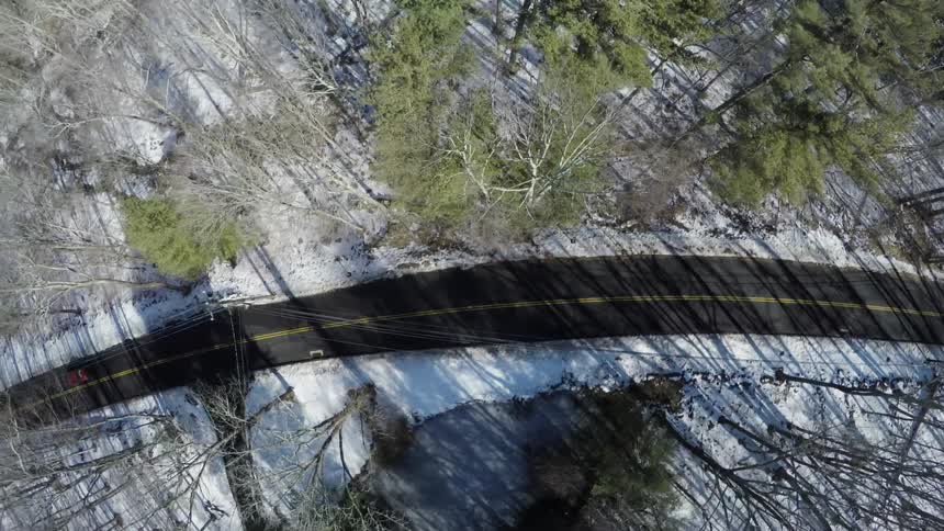 A vehicle drives down a narrow snow lined road through a forest