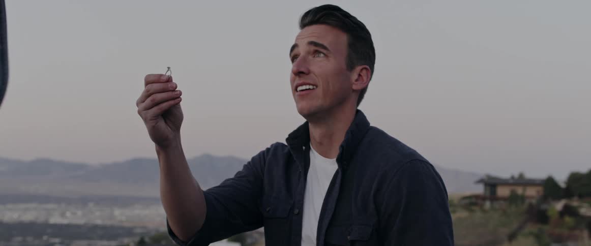 Man holds a ring as he proposes to his girlfriend outdoors who then jumps into his arms and they hug