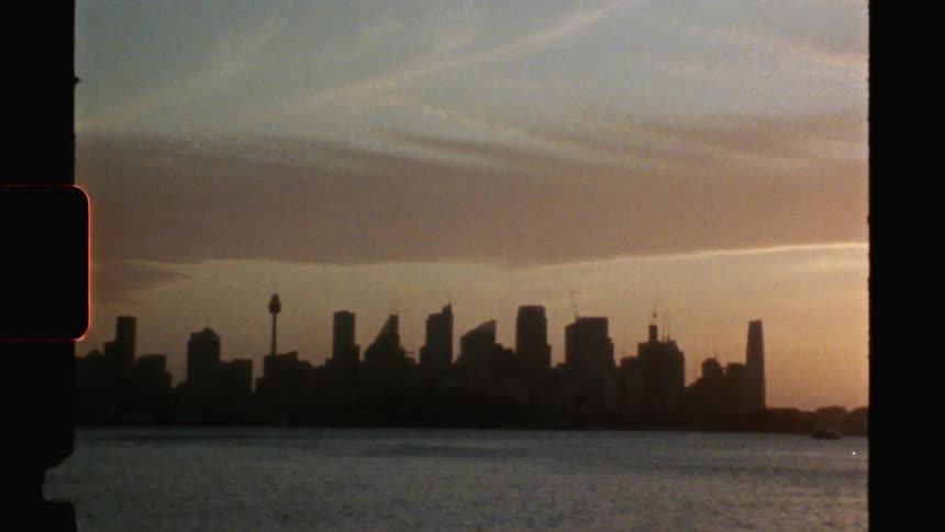 A slim tower stands in the city near the tall buildings near a lake
