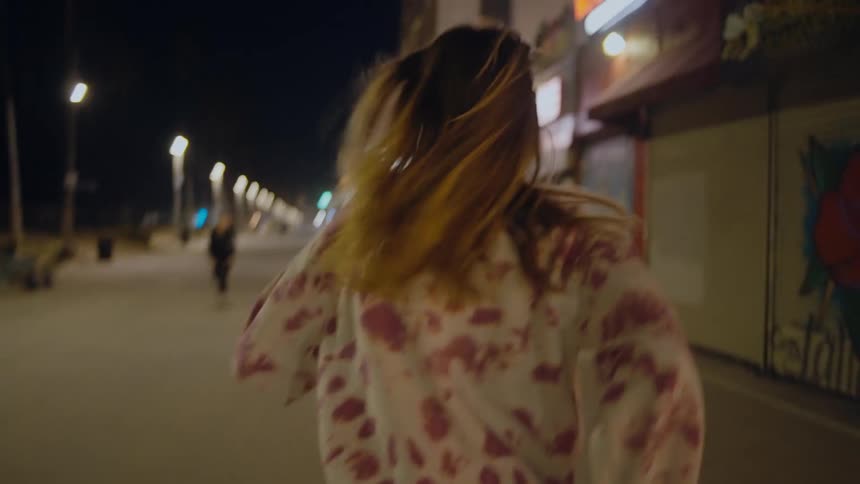 A woman with long hair is running on a city sidewalk at night