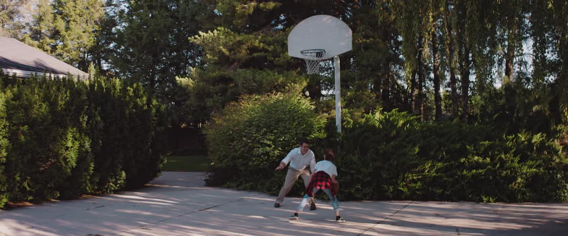 A dad plays basketball with his teenage daughter in their driveway after work