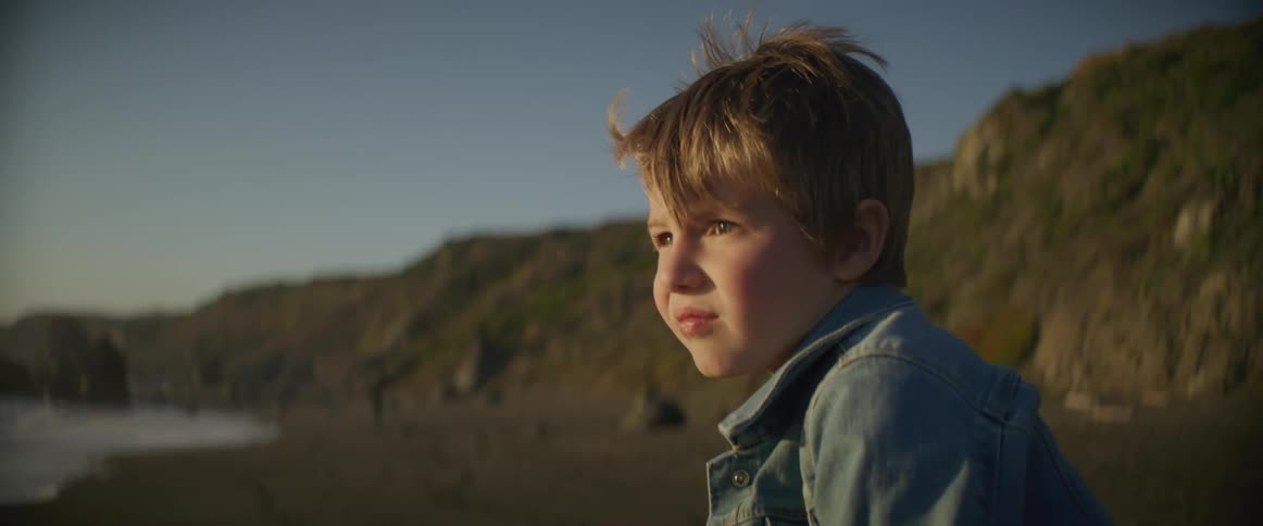 Boy with denim jacket watches the sea on the beach