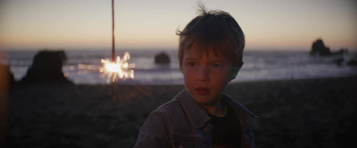 A young boy is standing on a beach holding a sparkler and watching the sparks
