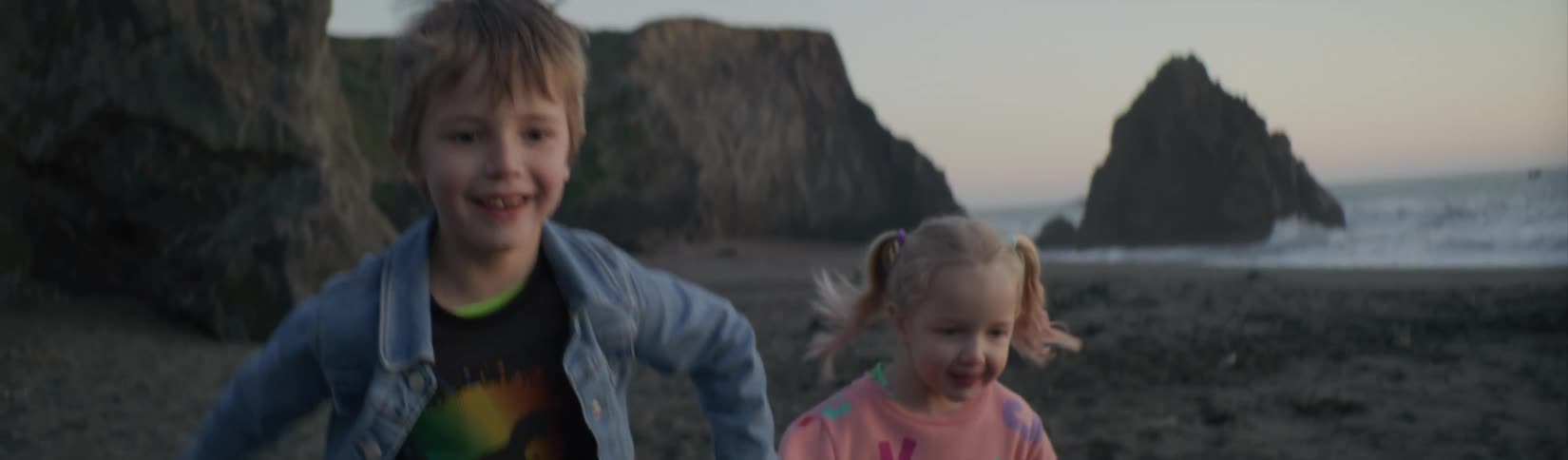 Happy brother and sister running on the sand on a beach holding hands near the ocean at evening
