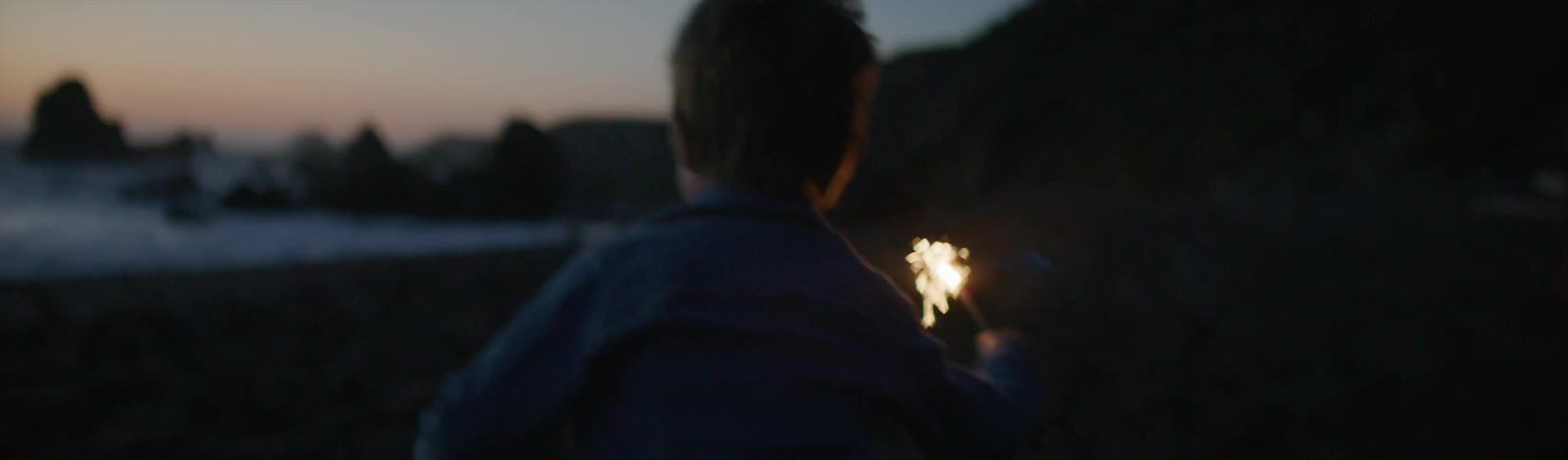 A young boy running with a burning sparkler outside at dusk