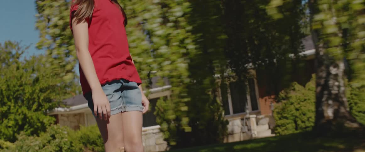 Girl with white helmet red t shirt shorts and white shoes skateboards in the street