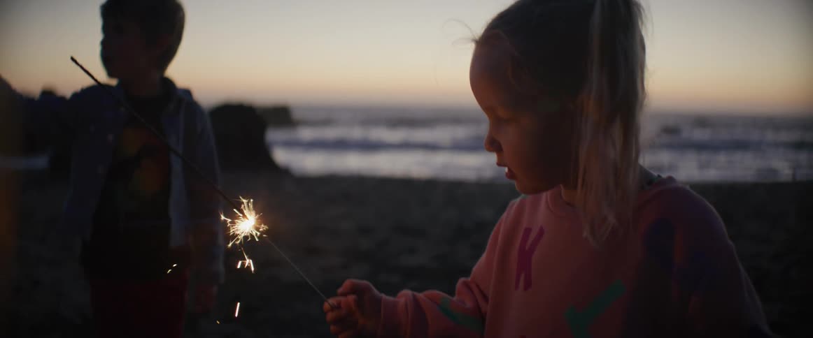 Brother and sister play with sparklers on the beach at night