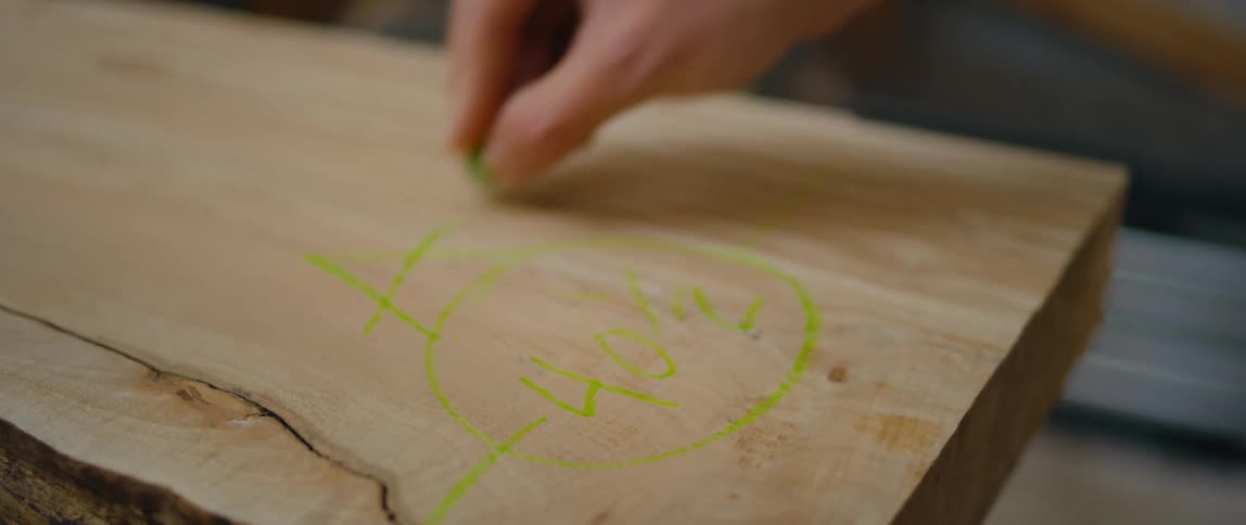 A man draws on a two by four with a green crayon