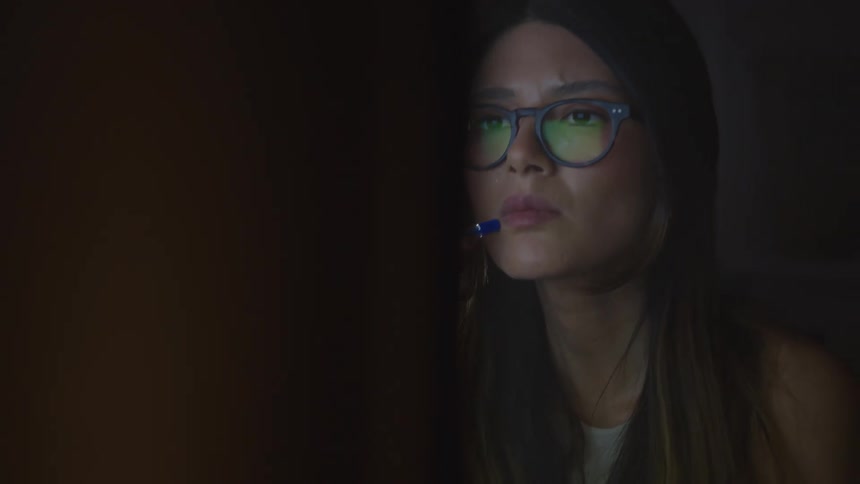 Woman sits at desk in front of computer entering numbers on a calculator as she looks at the screen