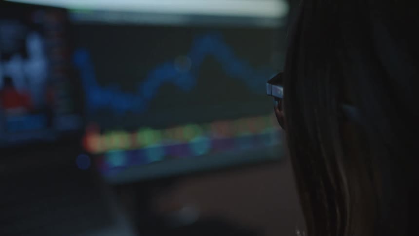 A woman turns her head to look at a monitor displaying a colorful line chart