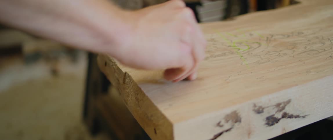 Person measures then marks thick wooden plank in workshop