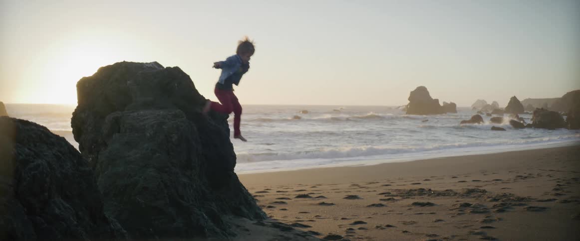 A child jumping off a rock on the beach