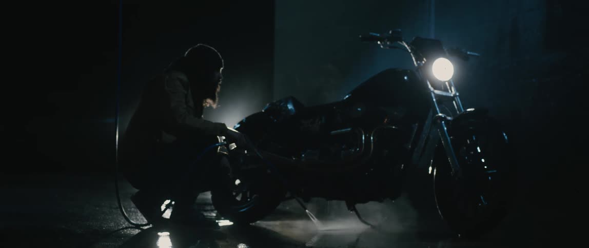 Bearded man holds running water hose as he cleans motorcycle in dark area