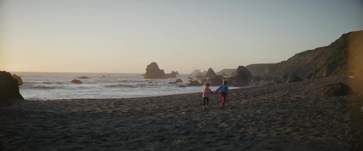 Boy and girl run on the beach at sunset next to the sea