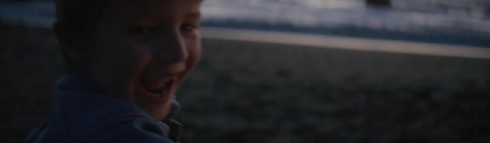 A boy laughs while waving a sparkler around on the beach