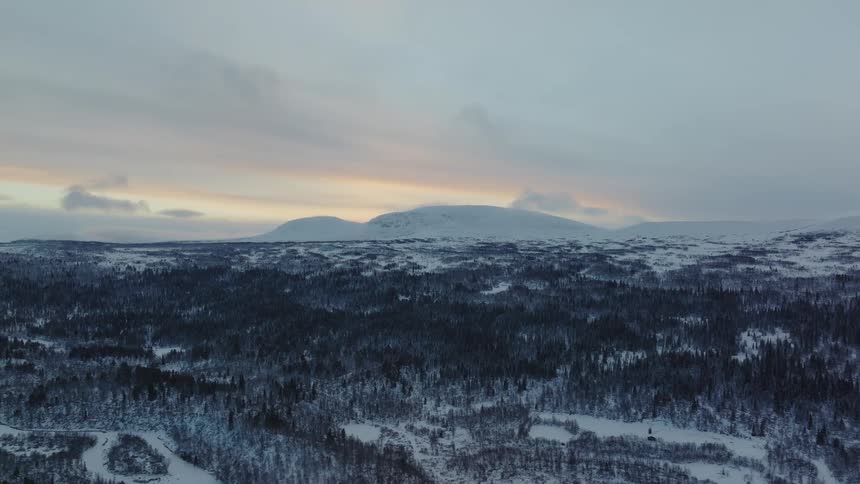 An aerial view of a snowy forest as the sun sets