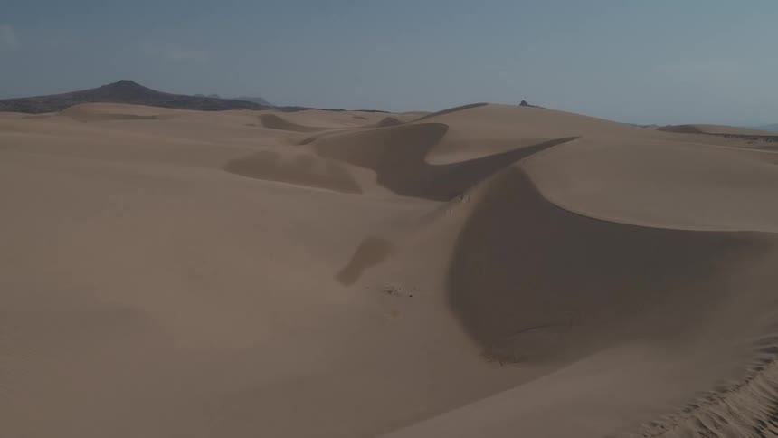 The sun shines upon drifted sand dunes in the desert