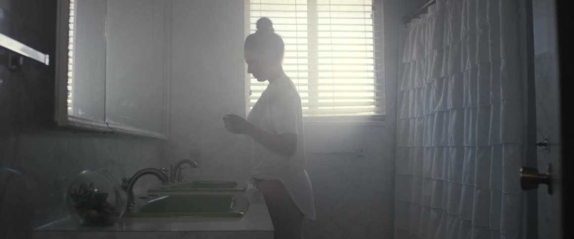 Woman with white shirt stands before the mirror holding pregnancy test