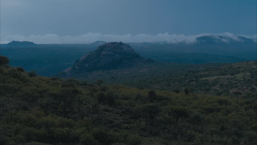 Mountains and a rocky hill sit near the grassy field