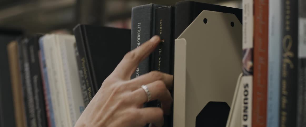 Two hands remove hardcover books from a bookshelf