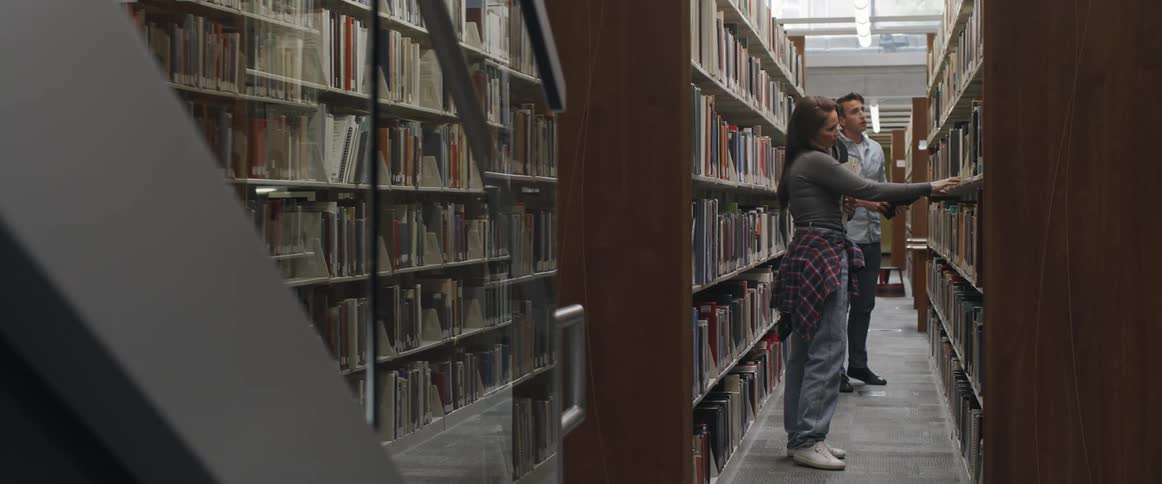 Two young college students searching books on the aisles of a library
