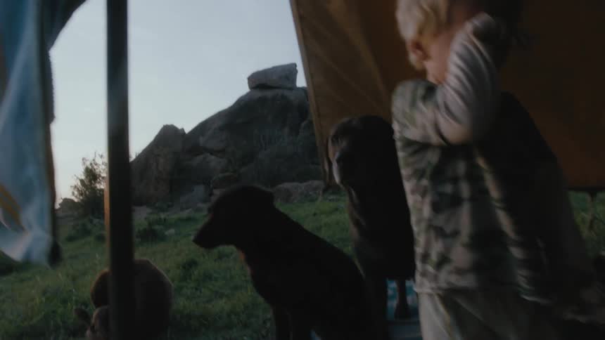 A man washes his face outside as he family sits nearby in a tent