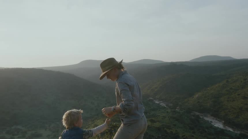 Woman wearing a sun hat standing on the edge of a cliff looking at the landscape view ahead and giving attention to a little boy